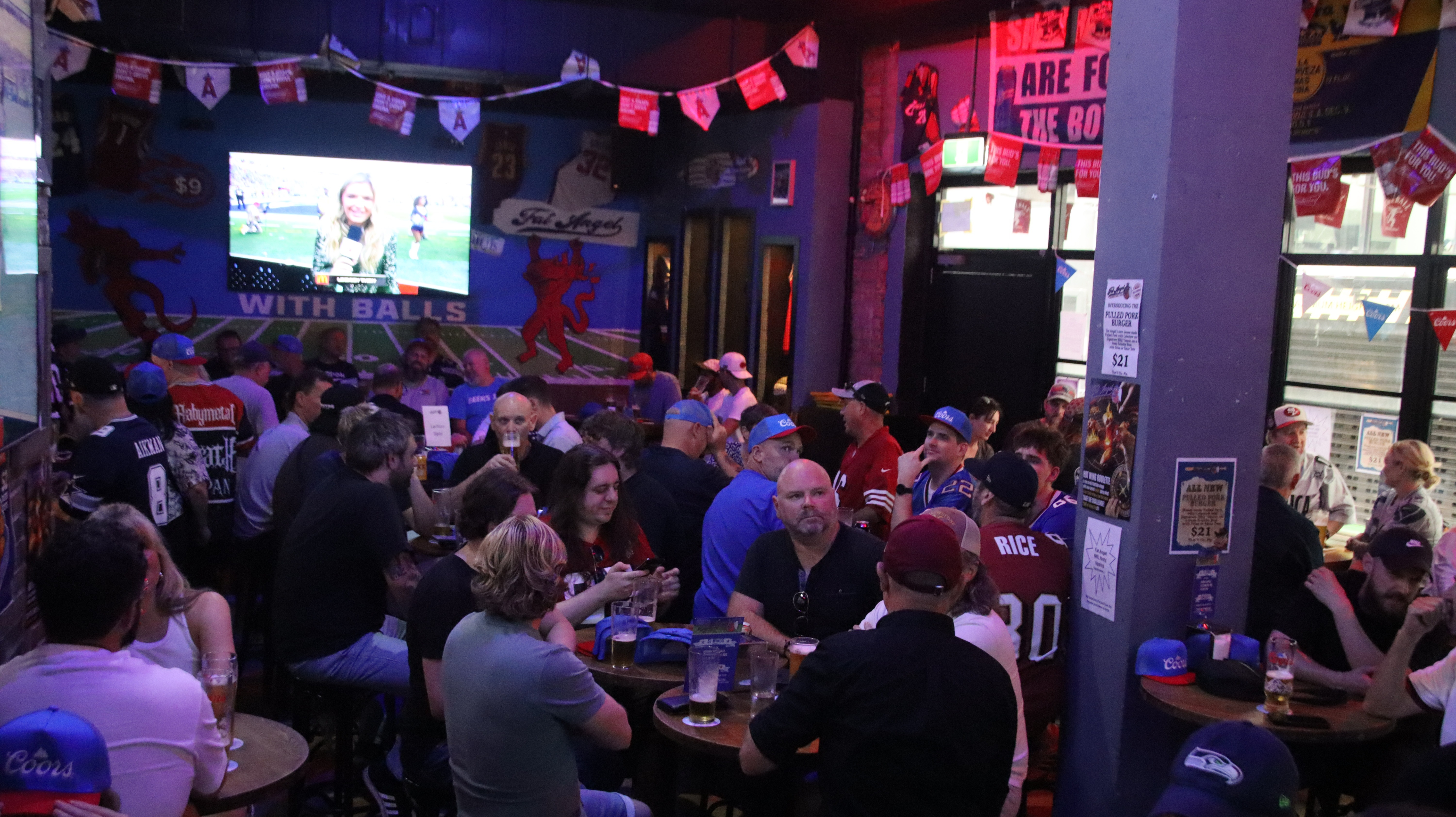 Packed crowd under the 'With Balls' field mural at Fat Angel